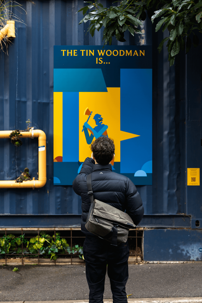 Person engaging with the Tin Woodman poster. The person is holding up their phone to the poster to view the augmented reality overlay.