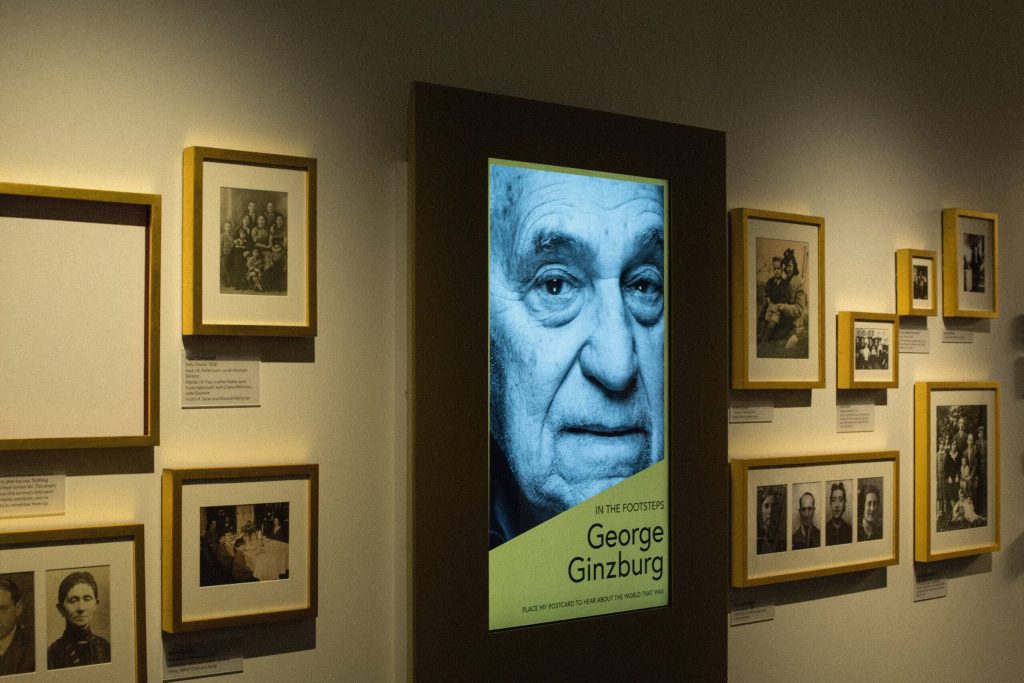 Framed photographs and a large screen on a wall of the gallery